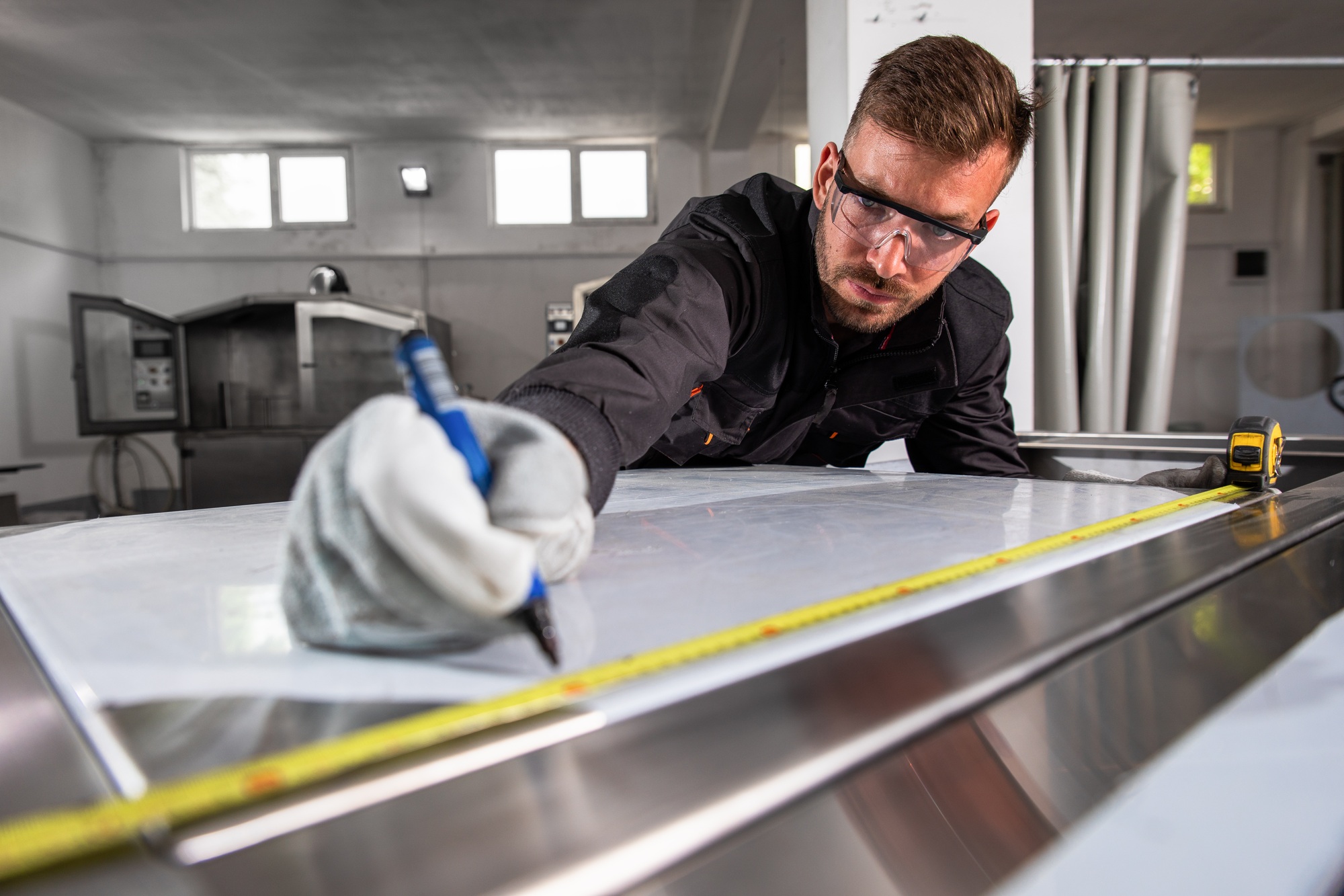 Industrial worker working on metal structure making marks with measuring meter at workshop.