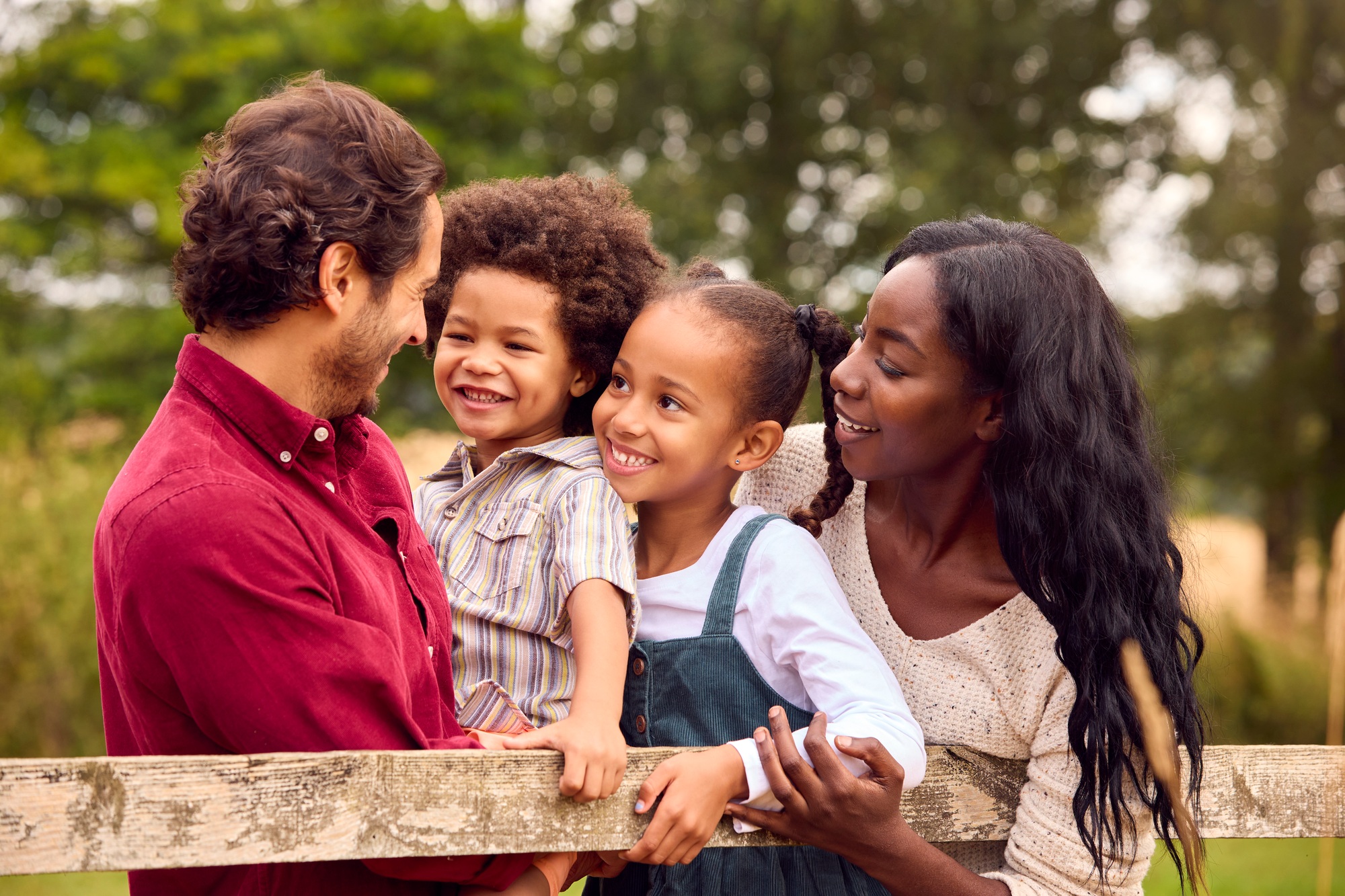 Loving Mixed Race Family Leaning On Fence On Walk In Countryside