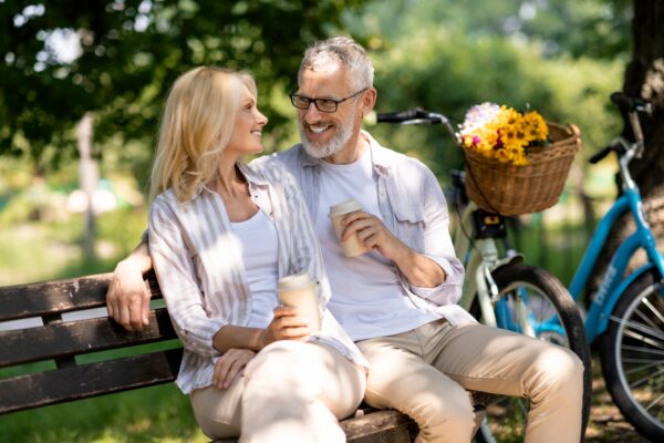 Romantic Mature Couple With Takeaway Coffee Relaxing On Bench In Summer Park