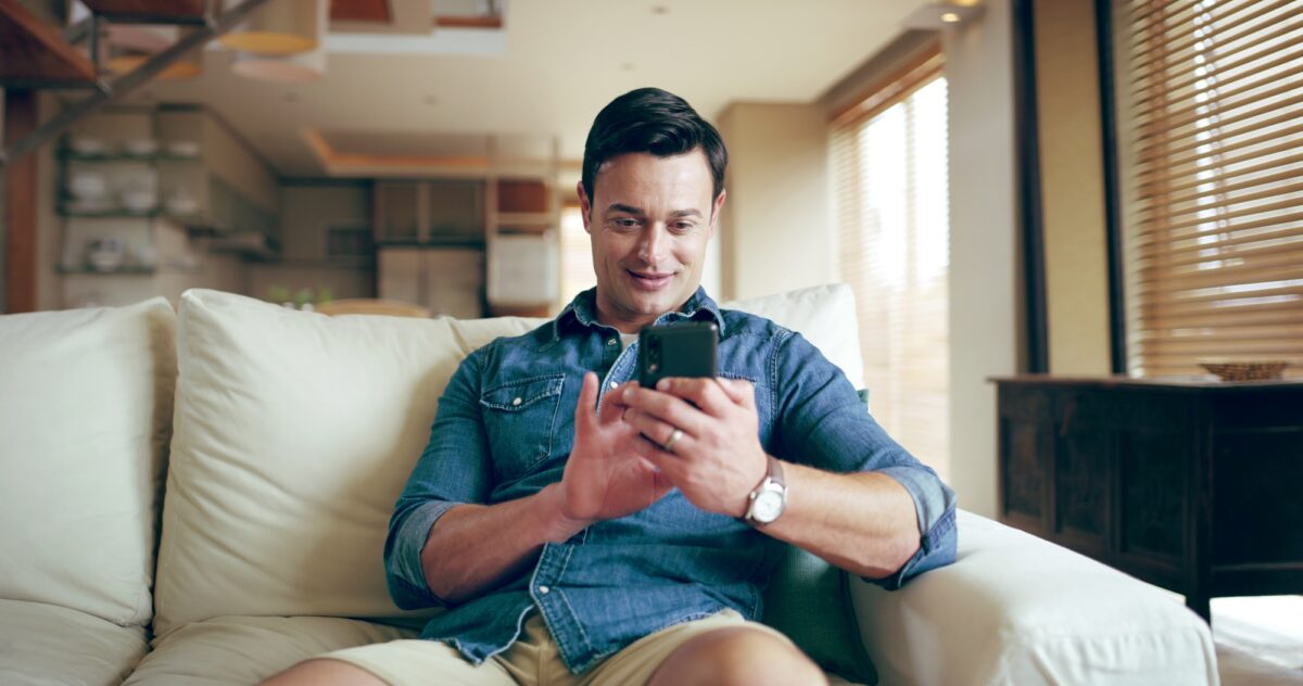 Sofa, man and smile with smartphone for chat, conversation and text message with contact at home. H