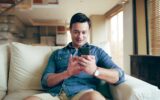 Sofa, man and smile with smartphone for chat, conversation and text message with contact at home. H