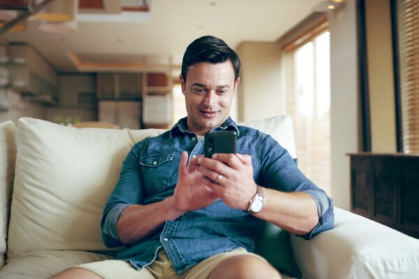 Sofa, man and smile with smartphone for chat, conversation and text message with contact at home. H