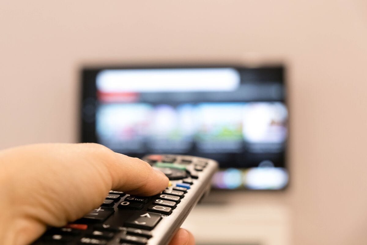 Watching TV and using remote controller. Hand holding TV remote control with a television in the