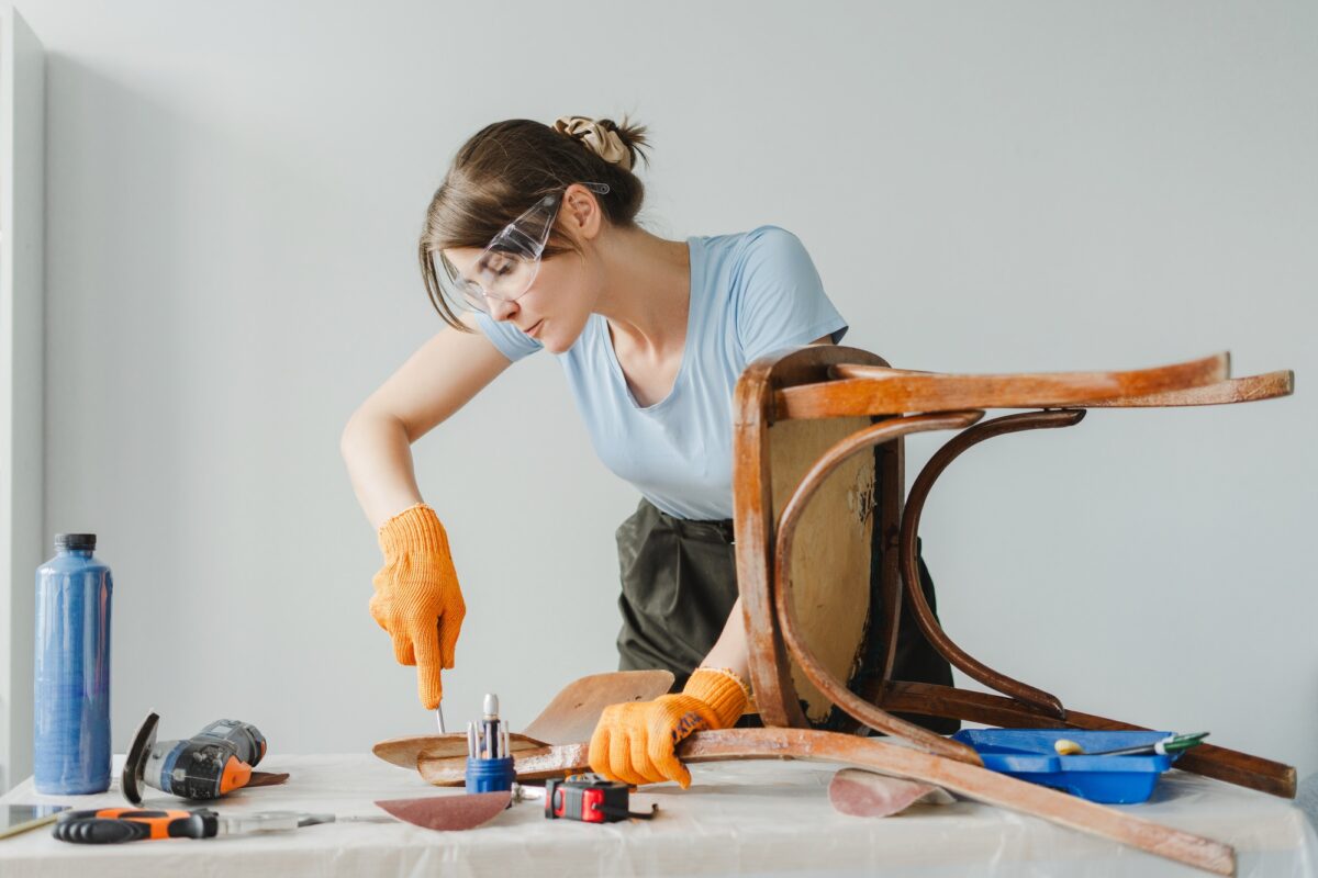 Woman using chisel restoring old wooden chair at home
