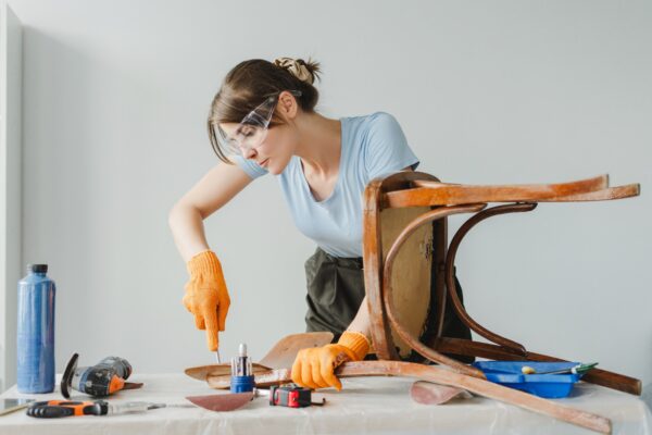 Woman using chisel restoring old wooden chair at home
