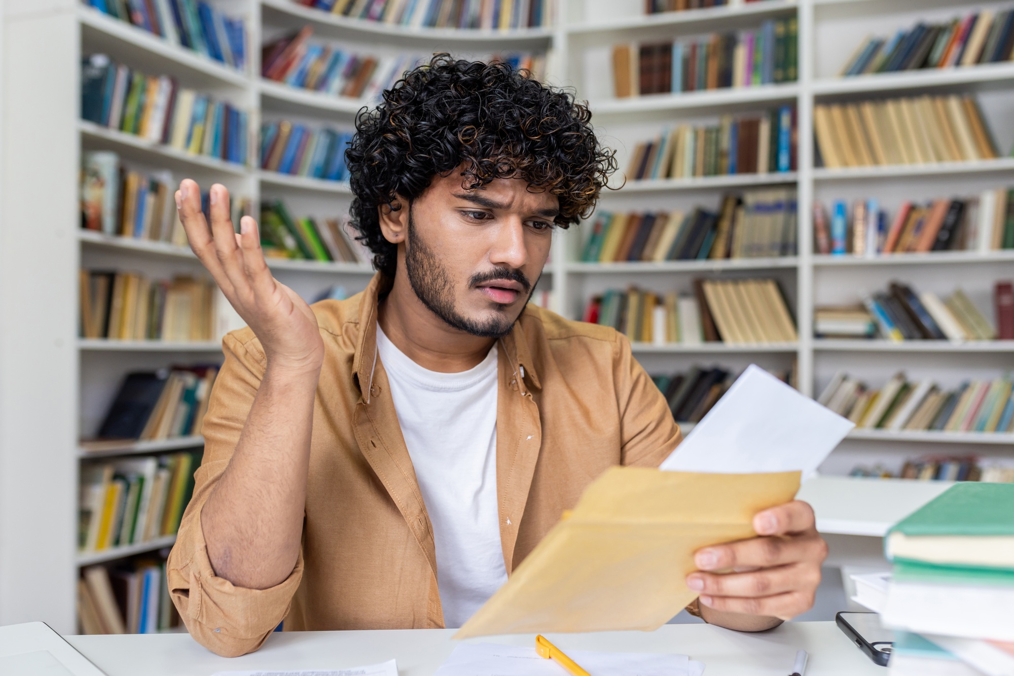 Young hispanic student upset studying inside university campus academic library, disappointed and