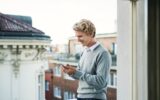 Young man with smartphone standing on a balcony in city, text messaging.